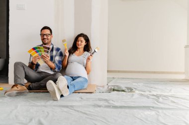 Hamile kadın ve kocası yeni dairenin duvarlarını boyamak için boya rengi seçiyorlar.