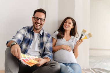 Hamile kadın ve kocası yeni dairenin duvarlarını boyamak için boya rengi seçiyorlar.