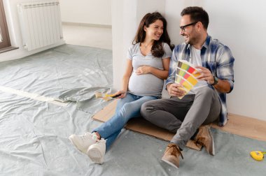 Hamile kadın ve kocası yeni dairenin duvarlarını boyamak için boya rengi seçiyorlar.