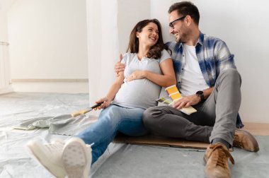 Hamile kadın ve kocası yeni dairenin duvarlarını boyamak için boya rengi seçiyorlar.