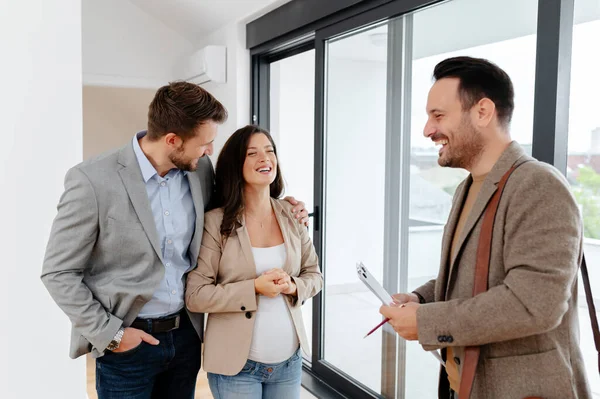 Man and his pregnant wife, talking with a real-estate agent visiting apartment for sale or for rent. Future parents buying an apartment. Real estate concept