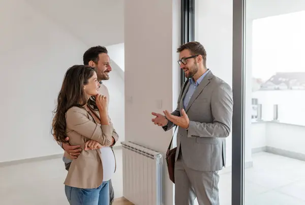 Man and his pregnant wife, talking with a real-estate agent visiting apartment for sale or for rent. Future parents buying an apartment. Real estate concept