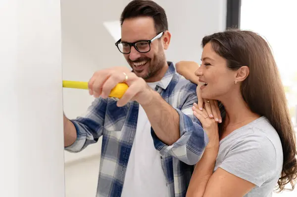 Bir adam ve hamile karısından oluşan genç, güzel ve neşeli bir çift, yeni ev yenileme projesinin bir parçası olarak duvarları ölçüyorlar.
