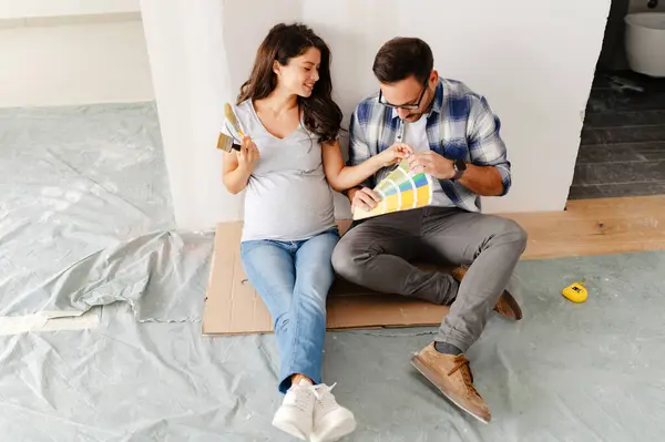 Hamile kadın ve kocası yeni dairenin duvarlarını boyamak için boya rengi seçiyorlar.