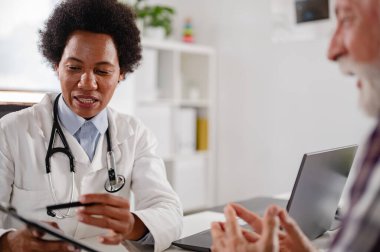 Doktor klinikte masada otururken hastayla konuşuyor. 