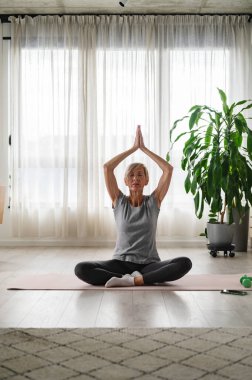 Yetişkin bir kadın oturma odasında meditasyon yapıyor. sağlıklı yaşam tarzı. 