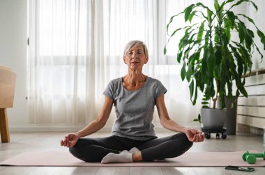 Yetişkin bir kadın oturma odasında meditasyon yapıyor. sağlıklı yaşam tarzı. 