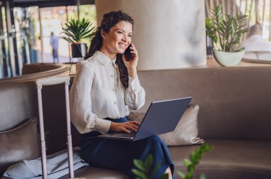 Bilgisayarı ve telefonu olan genç bir kadın otel lobisinde çalışıyor. 