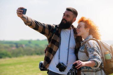 Mutlu çift dağlarda akıllı telefonlarıyla selfie çekiyor.