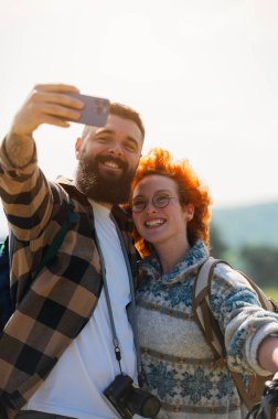 Mutlu çift dağlarda akıllı telefonlarıyla selfie çekiyor.