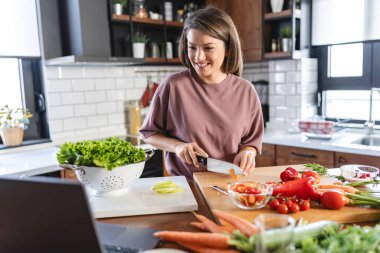 Mutfak masasında yemek hazırlayan gülümseyen kadın. Mutfakta salata yapan kadın..  