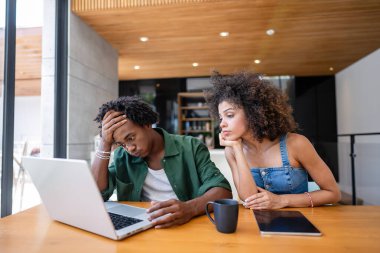 Gülümseyen genç Afrikalı Amerikalı çift evde dizüstü bilgisayar kullanıyor.