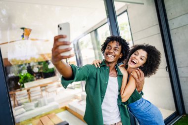 Modern bir dairede oturan genç bir çift cep telefonuyla selfie çekiyor.
