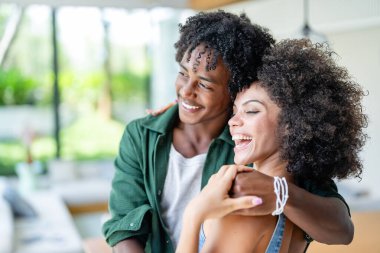 Gülümseyen Afrikalı Amerikalı kadın evde erkek arkadaşına sarılıyor.