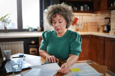 Gözlüklü kadın mutfaktaki masada dizüstü bilgisayar kullanıyor.