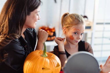 Mutlu anne ve kız aynaya bakıyor, cadılar bayramına hazırlanıyor.
