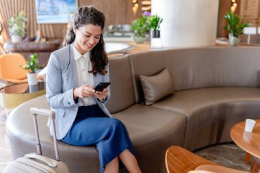 Gülümseyen iş kadını otelde akıllı telefon kullanıyor. 