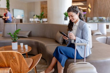 Gülümseyen iş kadını otelde akıllı telefon kullanıyor. 