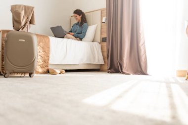 Genç bir kadın otel odasında yatarken dizüstü bilgisayarla çalışıyor.