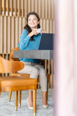 Güzel bir iş kadını otelde bilgisayarında çalışıyor ve kahve içiyor.