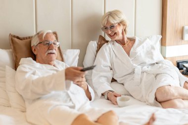 Mutlu çift otel odasında televizyon seyrediyor.