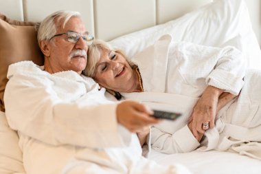 Otel odasında yatıp televizyon izleyen yaşlı çift. 