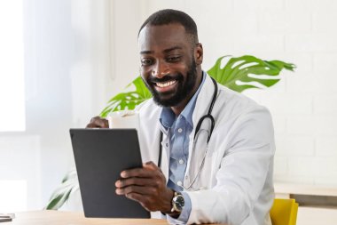 Afro-Amerikan doktor klinikte tablet kullanıyor.
