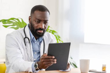 Afro-Amerikan doktor klinikte tablet kullanıyor.