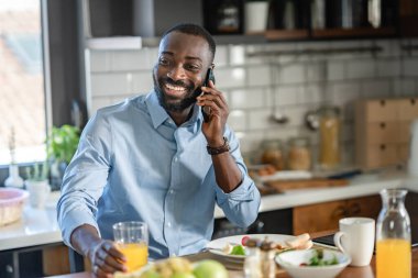 Genç siyah adam cep telefonu kullanırken kahvaltı yapıyor. 