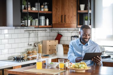 Evde kahvaltı yaparken tablet kullanan gülümseyen adam.