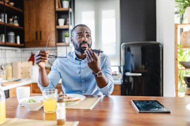 Genç Afrikalı Amerikalı adam kahvaltıda masada otururken telefon kullanıyor.  