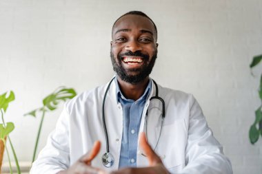 Klinikteki kameraya gülümseyen mutlu Afrikalı doktor.