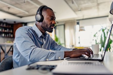 Bilgisayarda çalışan kulaklıklı genç bir erkek. 