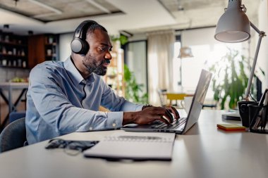 Bilgisayarda çalışan kulaklıklı genç bir erkek. 