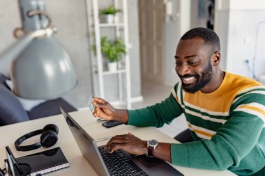 Genç Afrikalı gülümseyen ve elinde kredi kartı tutan bir adam online alışveriş yapıyor. 