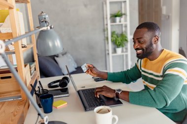 Afrikalı adam evde kredi kartıyla online alışveriş yapıyor. 