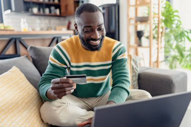 Afrikalı adam evde kredi kartıyla online alışveriş yapıyor. 