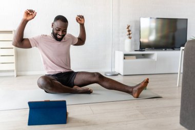 Afro-Amerikan adam evde egzersiz yapıyor, internette bilgisayar dersi alıyor. 