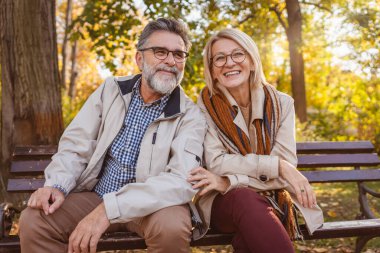 Kıdemli kadın ve erkek sonbahar parkında bankta oturuyor.