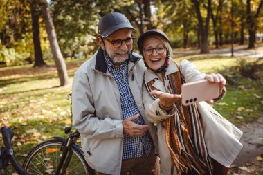 Sonbahar parkında selfie çeken olgun bir çift. 
