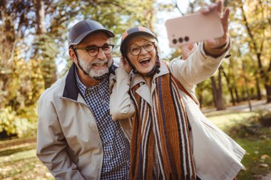 Sonbahar parkında selfie çeken olgun bir çift. 
