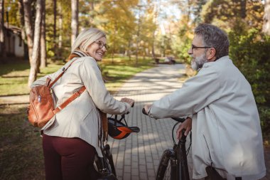 Parkta kocası olan yaşlı bir kadın bisiklet sürmeye hazırlanıyor. 