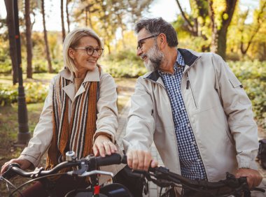 Sonbahar parkında bisiklete binmeye hazırlanan neşeli yaşlı çift. 