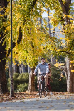 Sonbahar parkında bisiklet süren olgun mutlu bir çift. 