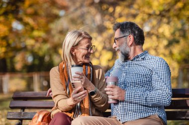 Mutlu olgun kadın ve erkek dışarıda kahve içerler.
