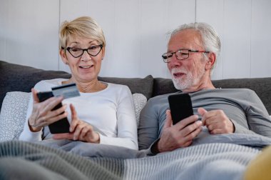 Yatakta cep telefonu kullanan yaşlı çift. 