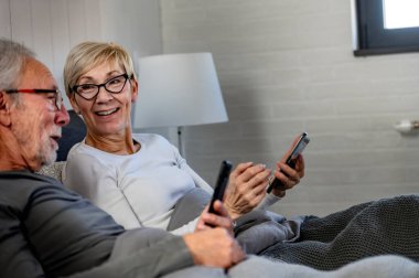 Yatakta cep telefonu kullanan yaşlı çift. 