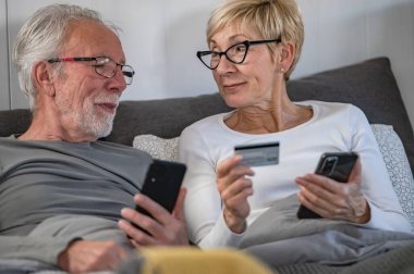 Kanepede alışveriş yaparken akıllı telefon ve kredi kartı kullanan mutlu çift.