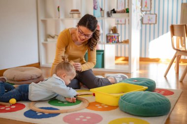 Öğretmen kız çocuğuna renkli bloklarla oynamayı öğretiyor.