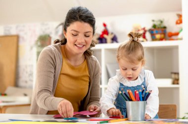 Küçük kız okulda öğretmeniyle resim yapıyor. 